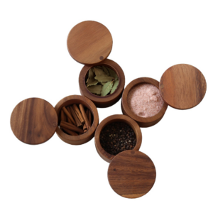 This image displays four of our Acacia Wood Salt Boxes with swivel tops containing four different items. Bay leaves, cinnamon sticks, pink salt, and black pepper.