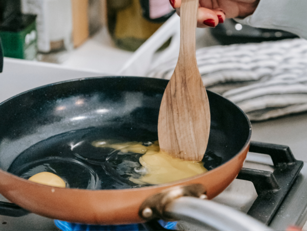 This image shows a wooden spoon being used in a non-stick pan to cook eggs. Displaying the soft properties of the wood, and showing that it indeed does not scratch non-stick coating or surfaces.