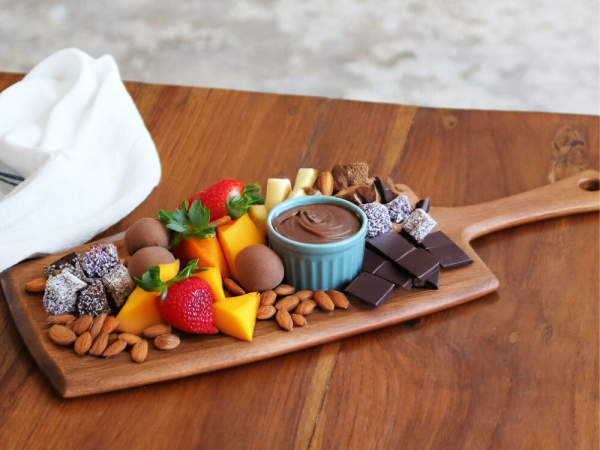 This image depicts a more out of the box charcuterie board idea. This board consists of various fresh fruits, peanut butter chocolate dip, chocolates, almonds, and some other assorted treats.